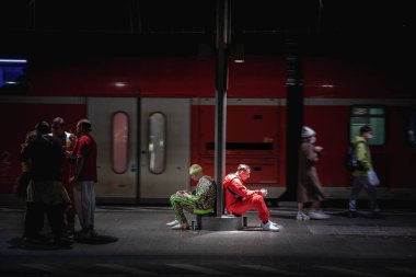 COLOGNE, GERMANY - 11 Kasım 2022: Köln Karnavalı 'nda Köln Hbf tren istasyonunda bekleyen akıllı telefon ve elektronik sigara içen spor kıyafeti giymiş erkekler için seçici bulanıklık.