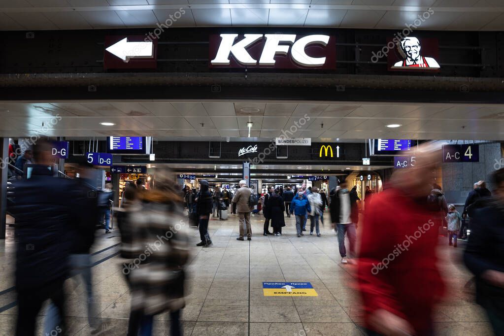 COLOGNE, GERMANY - NOVEMBER 6, 2022: Selective blur on passengers rushing in the concourse of Koln Hbf, Cologne Main train station (Hauptbahnhof) with the logo of KFC kentucky Fried Chichen fast food.
