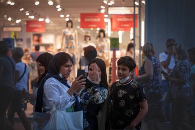 BELGRAD, SERBIA - 20 HAZİRAN 2021: Müslüman genç kadınlar, turistler, başörtüsü takan ve gece Belgrad sokaklarındaki bir akıllı telefondan birlikte video çağrısı yapan seçici bulanıklık.