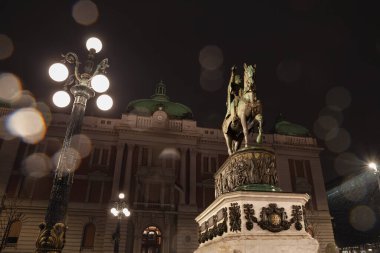 Yağmurlu bir akşamda, Sırbistan Ulusal Müzesi önünde Prens Mihailo (Knez Mihailo) heykeliyle Trg 'in Panoraması' nı gece bulanıklaştırır. Kod Konja olarak da bilinir, şehrin önemli bir simgesidir..