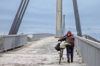 SREMSKA MITROVICA, SERBIA - 25 Şubat 2023: Yaşlı bir Sırp kadınında seçici bulanıklık, üst düzey, bisikletini ana yaya köprülerinden Sremska mitrovica 'nın en svetog irineja' sına itiyor.