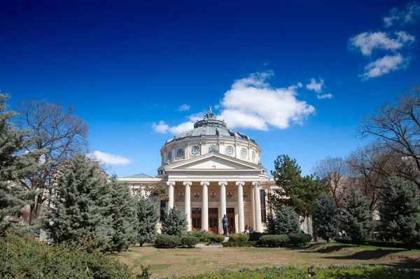 BÜKREŞ, ROMANIA - 18 Mart 2023: güneşli bir öğleden sonra bir parkın önündeki Roma ana cephesi. Romanya Atinası, Bükreş 'in önemli bir simgesi olan konser salonu ve mekanı.