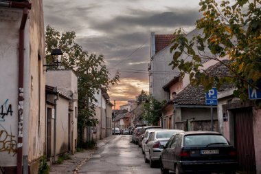 NOVI SAD, SERBIA - 15 Ekim 2022: Skerliceva ulica Caddesi Panorama, Podbara 'da şehir merkezi Novi Sad' ın dar bir caddesi, alacakaranlıkta arabaların park ettiği.