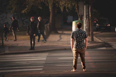 BELGRAD, SERBIA - 16 Ekim 2021: Sonbaharda Belgrad şehir merkezinde güneşli bir öğleden sonra Zebra geçidinde karşıdan karşıya geçmek için bekleyen genç bir adamın seçici bulanıklığı.