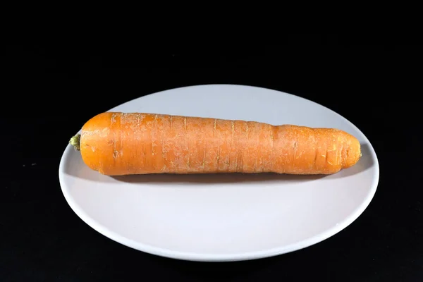 Orange carrot on a plate isolated on a black background in a studio shot, unpeeled, a single carrot, ready to be prepared.