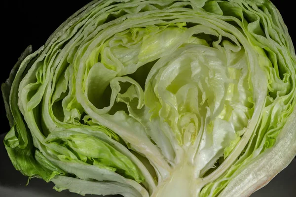 Selective blur on the heart of an iceberg lettuce, the core of a green salad, sliced and cut in half, isolated on a black background in a studio shot. iceberg is a species of lettuce.