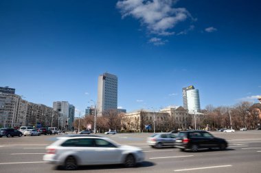 BUCHAREST, ROMANIA - 13 Mart 2023: Seçici bulanık arabalar, arka planda iş gökdelenleri ile Bükreş 'in zafer meydanı, Piata Victoriei Meydanı' nın yanından hızla geçen bulanık arabalar.