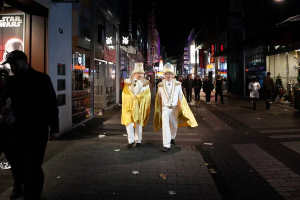 stock image COLOGNE, GERMANY - NOVEMBER 11, 2022: Selective blur on a group of two men, friends, german men dressed with white costumes for Cologne Carnival walking at night in Cologne center.