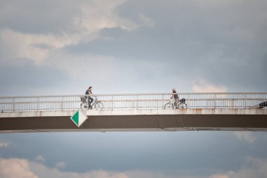 SREMSKA MITROVICA, SERBIA - 10 Haziran 2023: Erkekler Sava nehri üzerindeki bulutlu bir öğleden sonra, Sremska Mitrovica şehir merkezinde bisiklet sürüyor..