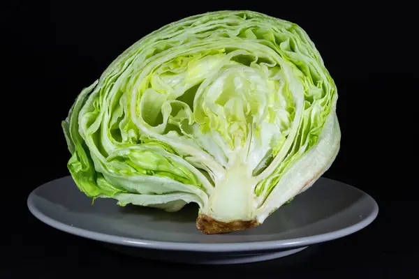Selective blur on an iceberg lettuce, the core of a green salad, sliced and cut in half, isolated on a black background in a studio shot on a grey plate. iceberg is a species of lettuce.