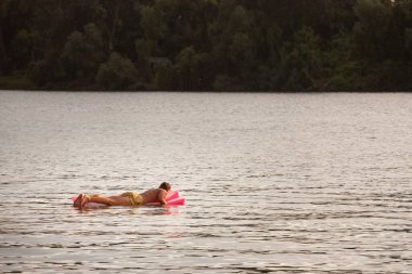 BELGRAD, SERBIA - 31 Temmuz 2021: Obrenovac 'taki Reka Sava Nehri' nde bir hava yatağında yüzen ve yüzen beyaz beyaz beyaz bir adam için seçici bulanıklık, alacakaranlık derecesi.