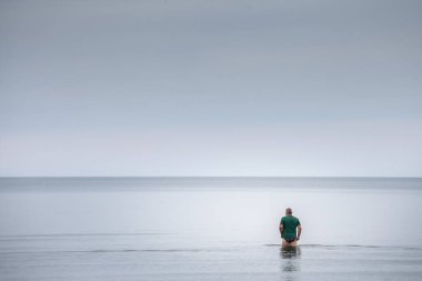 JURMALA, LATVIA - 26 AĞUSTOS 2023: Orta yaşlı bir adamın seçici bulanıklığı, Jurmala 'da soğuk denizde yıkanması, Letonya kıyılarında, Baltık denizinde suya girmeye çalışması.