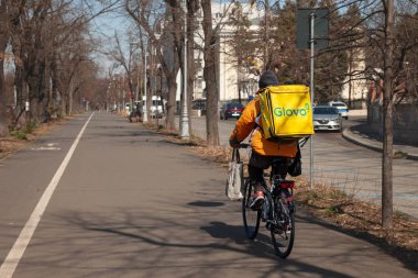 BUCHAREST, ROMANIA - 19 Mart 2023: Bükreş 'te bisikletli bir kuryenin çantasındaki Glovo logosu. Glovo, Avrupa 'da yayılmış bir İspanyol Gıda dağıtım uygulaması..