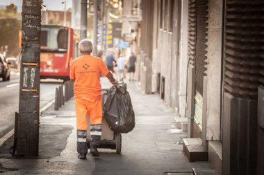 BELGRAD, SERBIA - 19 Temmuz 2022: Belgrad şehir merkezindeki sokakları süpürüp temizlerken çöp bidonunu çeken bir sokak temizleyicisi, bir yol süpürgesi üzerindeki seçici bulanıklık.