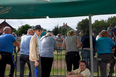 RUMA, SERBIA - 25 Haziran 2023: Sırp kırsalında kalabalığın önünde duran güneş gözlüğü ve şapka takan yaşlı adam. Sırp nüfusu yaşlanıyor.