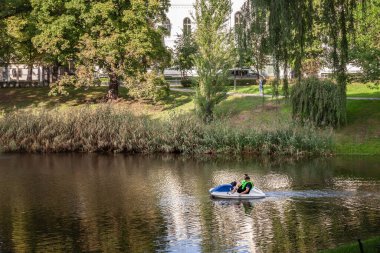 RIGA, LATVIA - 22 AUGSUT 2023: Bastejkalns Parkı 'ndaki Pilsetas Kanalları' nda (Riga Şehir Kanalı) pedal süren iki adam. Riga, Letonya 'da tarihi şehrin merkezini çevreleyen bir park..