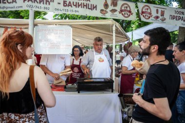 ERDEVİK, SERBIA - 25 Haziran 2023: Sırbistan 'da bir pazarda, Balkanlar' da geleneksel bir barbekü olan Rostilj 'de, pljeskavica adı verilen et ve köfte ızgara yapan bir kalabalık.