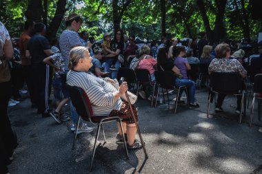 ERDEVİK, SERBIA - 28 Haziran 2023: Sırbistan 'ın Erdevik kentindeki bir topluluğun ortasında yaşlı bir kadın, bir büyükanne, oturmuş ve eğleniyor.