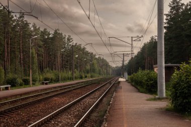 Tipik bir doğu Avrupa tarzı Rus demiryolu altyapısının panoraması: Letonya 'da gün batımında bir tren istasyonu bulunan Pabazi tren istasyonundaki bir Letonya ormanında elektrikli demiryolu hattı.
