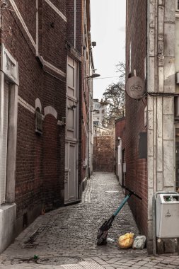 LIEGE, BELGIUM - 9 Kasım 2022 Dar ve kirli bir liege caddesinde elektrikli scooter 'da seçici bulanıklık, Belçika' da, yayada, çöp torbalarıyla.