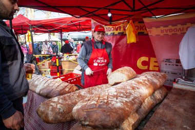 KACAREVO, SERBIA - FEBRUARY 13, 2024: baker on a serbian market selling giant bread in loaf, in Kacarevo, sliced or in full sized, also called hleb in Serbian. clipart