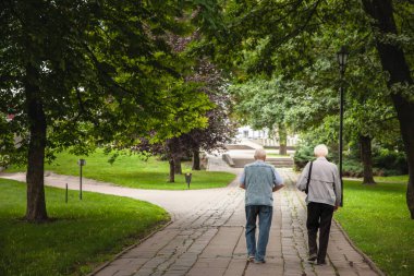 JELGAVA, LATVIA - AUGUST 18, 2023: Selective blur on two old men, friends, latvian, walking together in a park in Jelgava in summer. Latvian population is ageing. clipart