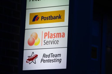 AACHEN, GERMANY - NOVEMBER 8, 2022: Entrance of a german office at night with the logo of German bank postbank, plasma service, a plasma management firm, and redteam pentesting, cybersecurity cabinet. clipart