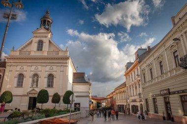 PECS, HUNGARY - 21 Eylül 2023: Saint Sebastian Kilisesi (Szent Sebestyen vertanu templom) irgalmasok utcaja caddesinde öğleden sonra insanlar yürürken. Pecs 'in yaya sokağı..