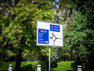 Letonya 'nın Riga ve çeşitli yerel noktalarının yönlerini gösteren yol işaretleri üzerindeki seçici bulanıklık: Letonya' daki Eleja, Riga, Sauli / Siaulai, Dobele, Tukums ve Sigulda Merkezi (merkezler).