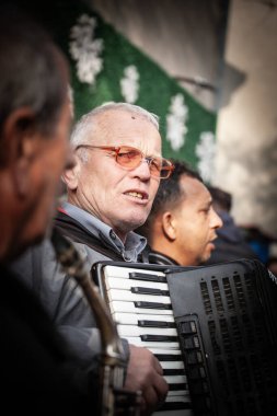 KACAREVO, SERBIA - FEBRUARY 21, 2024: Kacarevo 'da, geleneksel Sırp pazarı olan slaninijada' da, Kacarevo 'daki diğer Balkan müzik çalanlarının önünde akordeon çalan bir akordeoncunun seçici bulanıklığı.