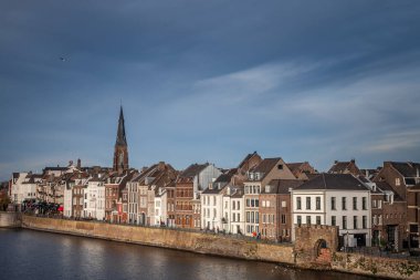 MAASTRICHT, NETHERLANDS - NOVEMBER 10, 2022: Panorama of Maastricht Waterfront on the Meuse Maas river with a focus on the Sint Martniuskerk, a catholic church and typical dutch architecture houses. clipart