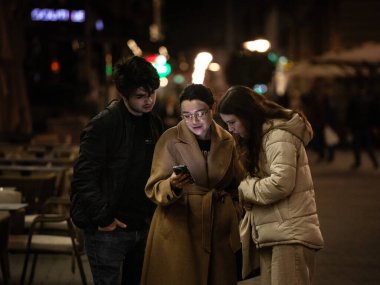 BELGRAD, SERBIA - 10 Şubat 2024: Geceleri Belgrad sokaklarında akıllı bir cep telefonunu birlikte izleyen üç kişi, genç ve genç Sırp 'ta seçici bulanıklık.