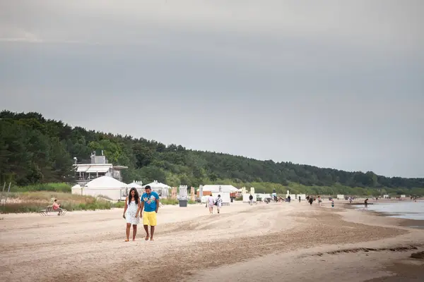 stock image JURMALA, RIGA - AUGUST 25, 2023: Selective blur on a couple, lovers, walking on a beach in Jurmala Pludmale, in front of a Latvian forest in the baltic sea.