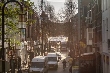 HEERLEN, NETHERLANDS - 10 Kasım 2022: seçici bulanıklık Heerlen Saroleastraat caddesinde şafak vakti ışığa doğru, ana cadde, teslimat kamyonları, atölyeler ve daireleri olan yayalar.