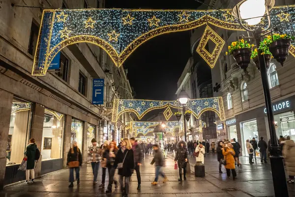 stock image BELGRADE, SERBIA - DECEMBER 9, 2023: Selective blur on a Crowd walking at night on Kneza Mihailova street with shops in old town decoration and illuminated for New Year and Christmas.