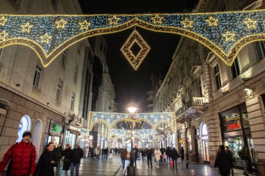 BELGRAD, SERBIA - 21 ARALIK 2023: Kneza Mihailova caddesinde geceleri yürüyen ve eski kasaba dekorasyonunda dükkanları olan seçici bulanıklık ve yılbaşı ve Noel için aydınlatılmış.