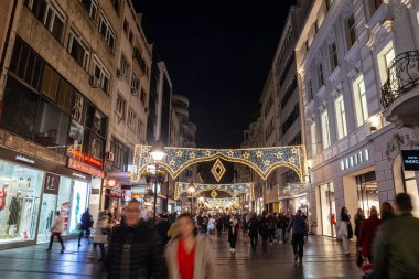 BELGRAD, SERBIA - 9 ARALIK 2023: Kneza Mihailova caddesinde geceleri yürüyen ve eski kasaba dekorasyonunda dükkanları olan seçici bulanıklık ve yılbaşı ve Noel için aydınlatılmış.