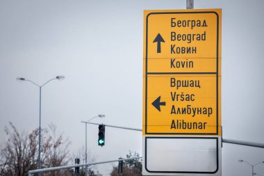 Çeşitli varış noktalarını gösteren bir Sırp yol tabelasının fotoğrafı. Tabela, hem Latince hem de Kiril alfabesiyle Beograd, Kovin, Vrsac ve Alibunar 'a giden yönleri gösteriyor ve Sırpça işaretlerin iki dilli doğasını vurguluyor..