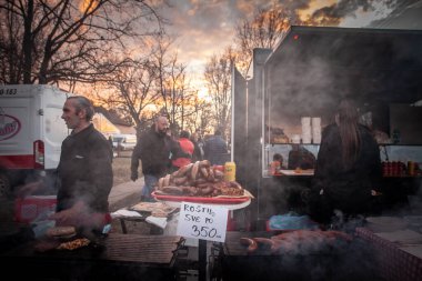 BELO BLATO, SERBIA - 18 Şubat 2024: Balkanlar 'da geleneksel bir Rostilj barbeküsü olan Sırbistan' da bir pazarda dumanla ızgara yapan Sırp sosisleri.
