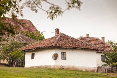 Geleneksel bir Balkan evi ile Sırbistan 'ın kırsal kesimindeki eski ve yeninin karışımını vurgulayan modern bir uydu anteni arasındaki zıtlığı gösteren bir resim.