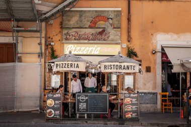 ROME, ITALY - 14 Haziran 2024: Roma 'da geleneksel İtalyan pizzacısı ve restoranının açık hava manzarası, yemek masaları ve şemsiyeler altında yemeklerin keyfini çıkaran insanlar.