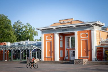 SIGULDA, LATVIA - 15 AĞUSTOS 2023: Letonya 'daki Sigulda tren istasyonunun (diğer adıyla Siguldas Stacija) önünde bisikletiyle duran adam. Sigulda, Riga 'nın doğusunda bir şehirdir..