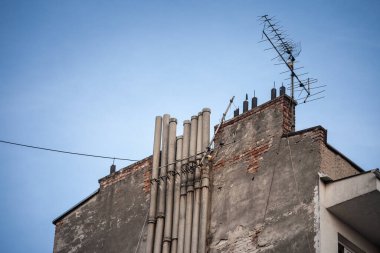 Kentsel ortamda çürüyen bacaları olan eski bir bina, zamanın ve kirliliğin şehir altyapısı üzerindeki etkilerini egzoz boruları ve baca dumanıyla vurguluyor..