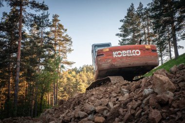 DIVCIBARE, SERBIA - JULY 22, 2022:A weathered Kobelco excavator operates in a rugged construction site in Divcibare, Serbia. Kobelco is a japanse machinery company specialized in industrial vehicles. clipart