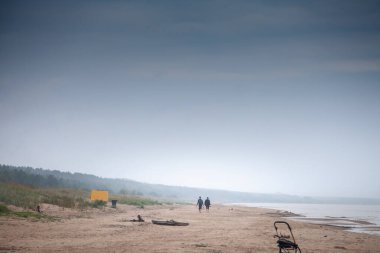 GARCIEMS, LATVIA - AUGUST 24, 2023: Two people walking on the quiet beach of Garciems by the Baltic Sea in Latvia. Garciems is a sea resort of Latvia in baltic states. clipart