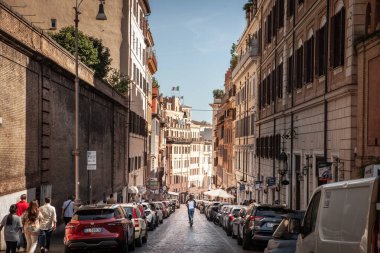 ROME, ITALY - 14 Haziran 2024: Roma 'nın tarihi merkezinde dar bir cadde boyunca hareket eden elektrikli scooter kullanan turistler, tipik İtalyan mimarisinin eski binalarıyla çevrili..
