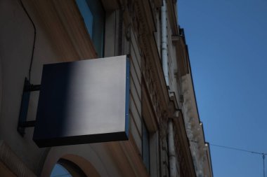 Bir bina cephesinde asılı boş mavi kare tabela, Avrupa şehir caddesinde berrak bir gökyüzüne karşı görünür, perakende ticaret reklamcılığı ve kentsel ticari bilgi ekranı için ideal.