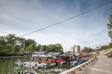 PANCEVO, SERBIA - OCTOBER 12, 2023: Tamis Quay in Pancevo, Serbia, with small boats docked by the river and people dining at a riverside restaurant. Pancevo is a serbian city in banat. clipart