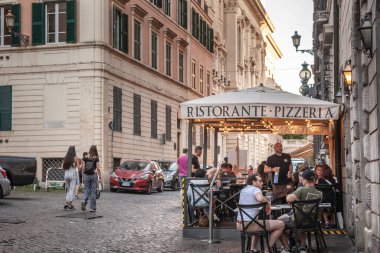 ROME, ITALY - JUNE 15, 2024: People enjoy dining on terrace of a traditional pizzeria restaurant in the old town capturing the essence of Italian cuisine & social atmosphere of Rome historic streets.