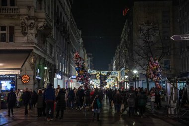 BELGRADE, SERBIA - DECEMBER 21, 2024: Selective blur on a Crowd walking at night on Kneza Mihailova street with shops in old town decoration and illuminated for New Year and Christmas. clipart